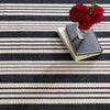 Birmingham Black Woven Cotton Rug styled with books and red flowers. Styled view.
