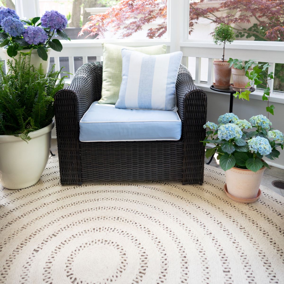 Bowline Natural Indoor/Outdoor Round Rug styled in a sunroom with wicker chair and outdoor planters. Styled view.