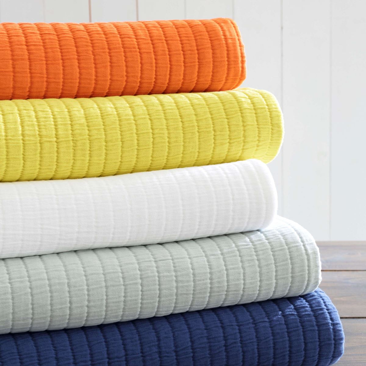 Folded stack of coverlets in multiple colours. Styled view.