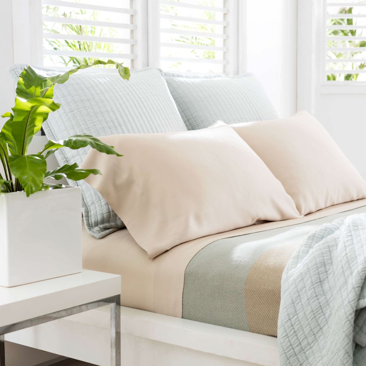 Light pink and light blue pillows on a made up bed. Styled view.