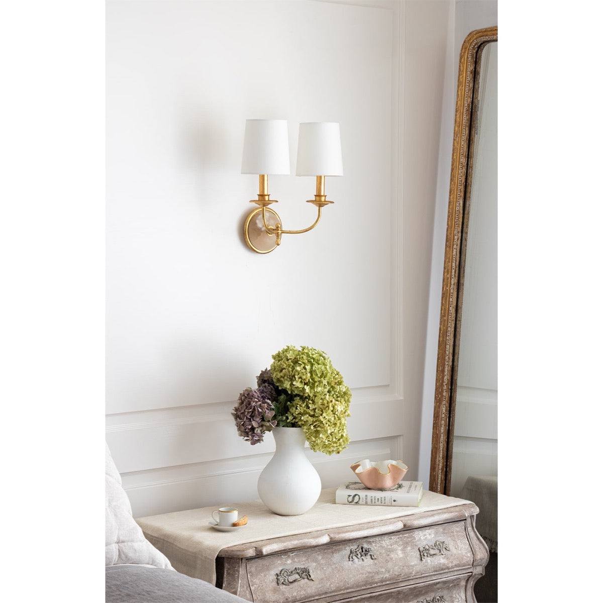 Fisher Double Sconce styled on a white wall above an antique night stand. Styled view.