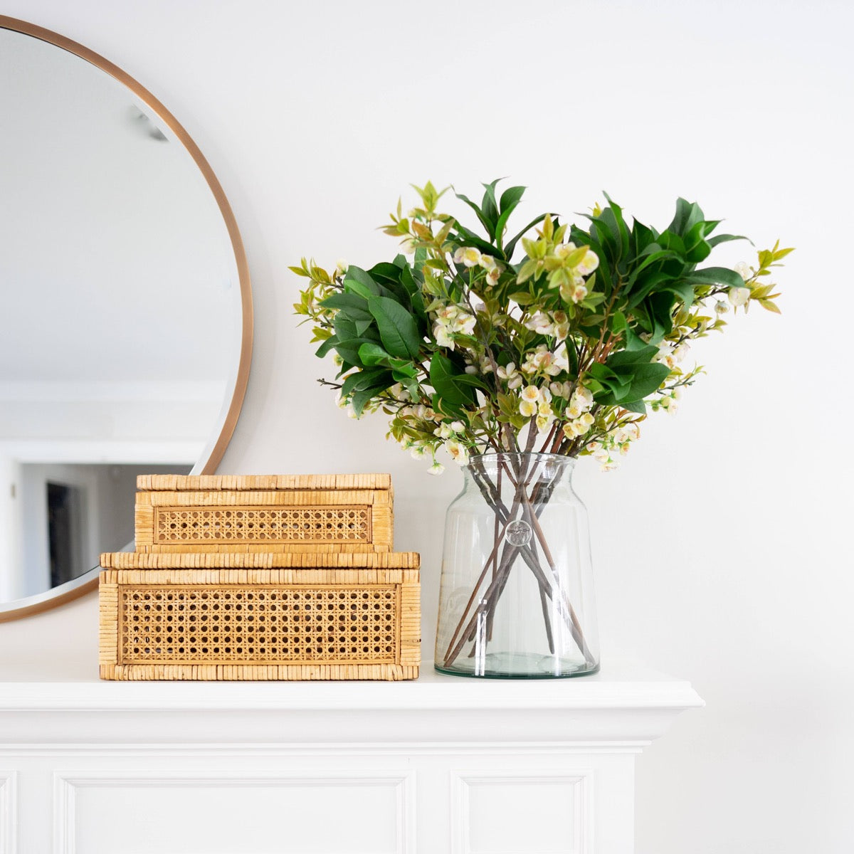 Carrie Mirror styled above a white mantel with brown wood boxes and greenery. Styled view.