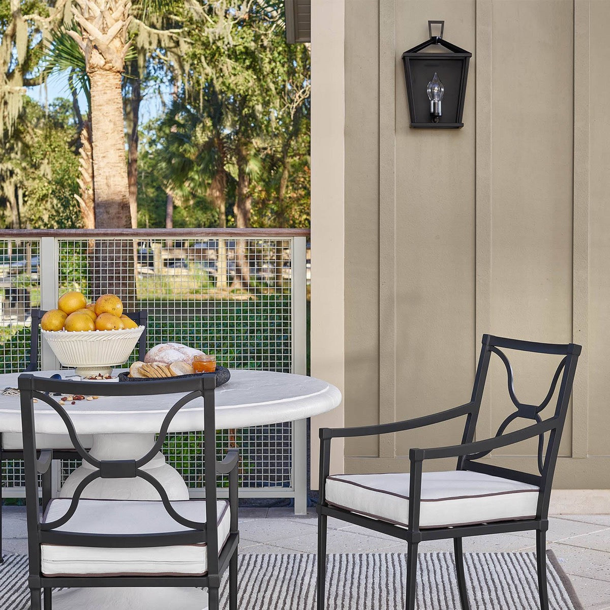 Hampton Outdoor Sconce styled on a panel wall with outdoor furniture. Styled view.