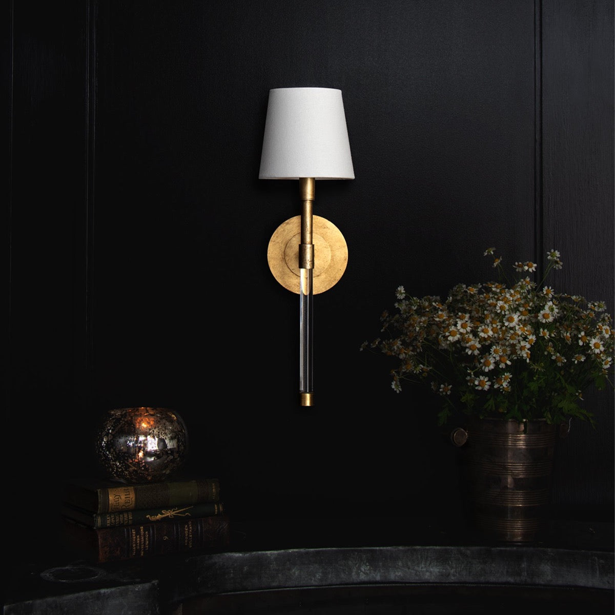 Auburn Crystal Sconce styled on a black wall with books and greenery. Styled view.