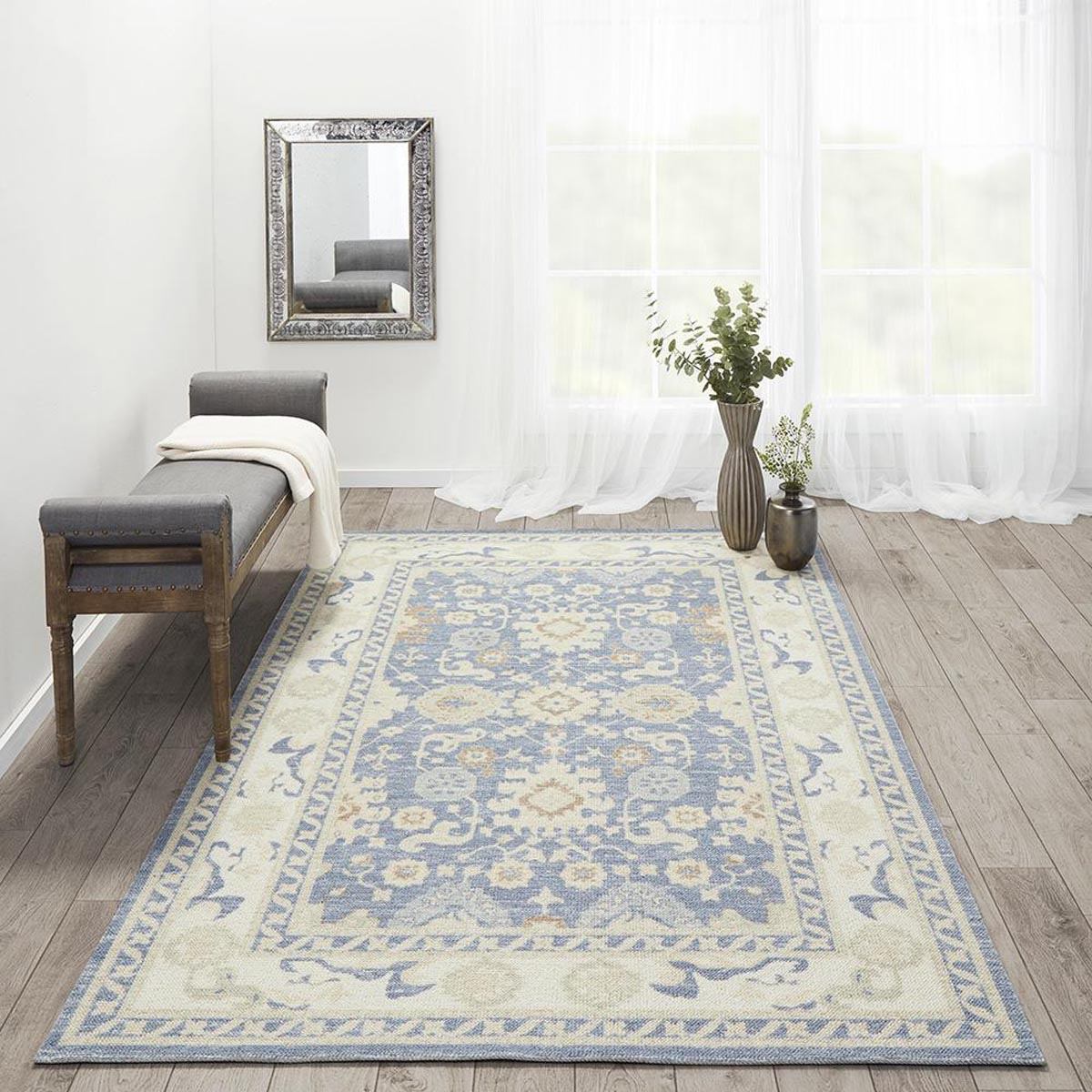 Ellesworth Rug styled with a mirror, bench and greenery. Styled view.