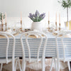 Harwich Natural Woven Jute Rug styled under an blue cloth dining table with white chairs and spring decor. Styled view.