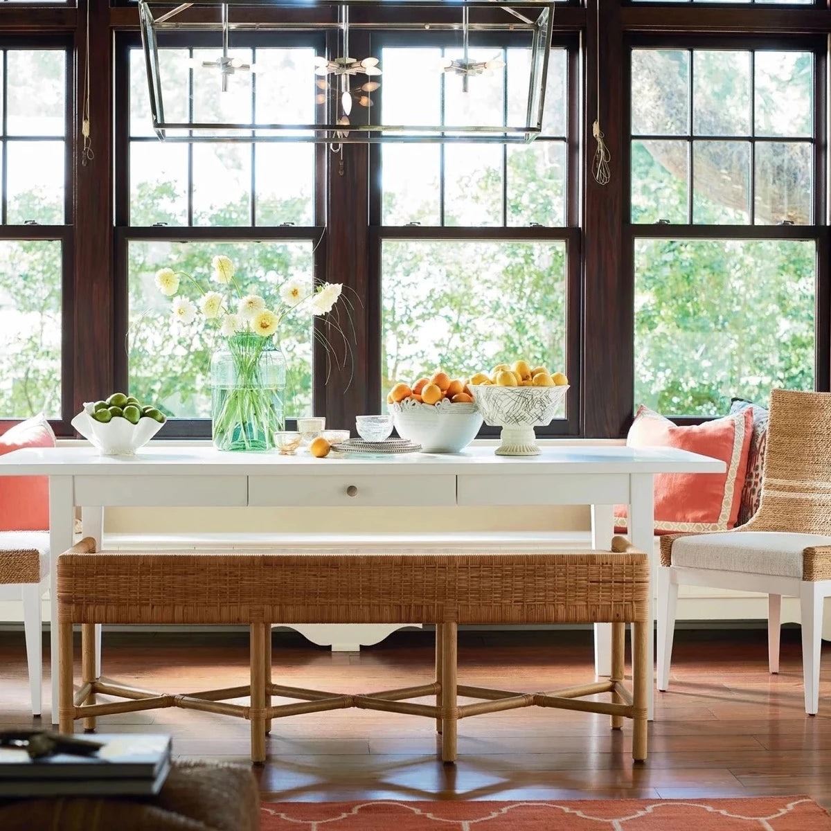 Heidi Bench styled with a white dining table and wicker chairs in front of large windows. Styled view.