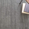 Herringbone Black Woven Cotton Rug styled under books. Styled view.