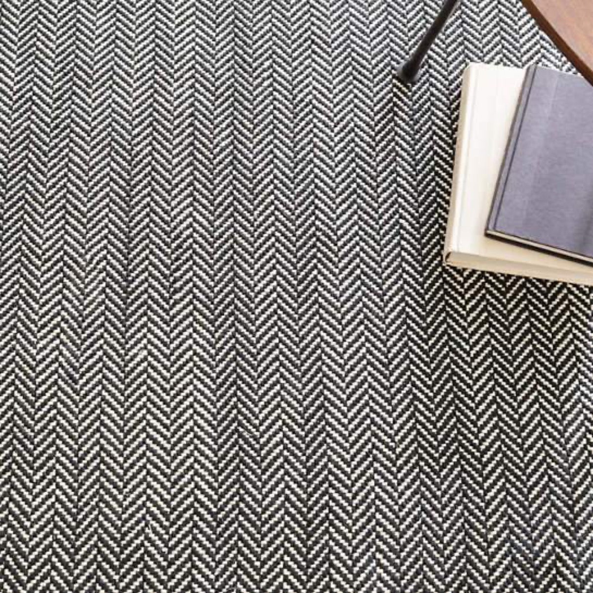Herringbone Black Woven Cotton Rug styled under books. Styled view.