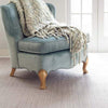 Herringbone Dove Grey Woven Cotton Rug styled under a blue chair. Styled view.