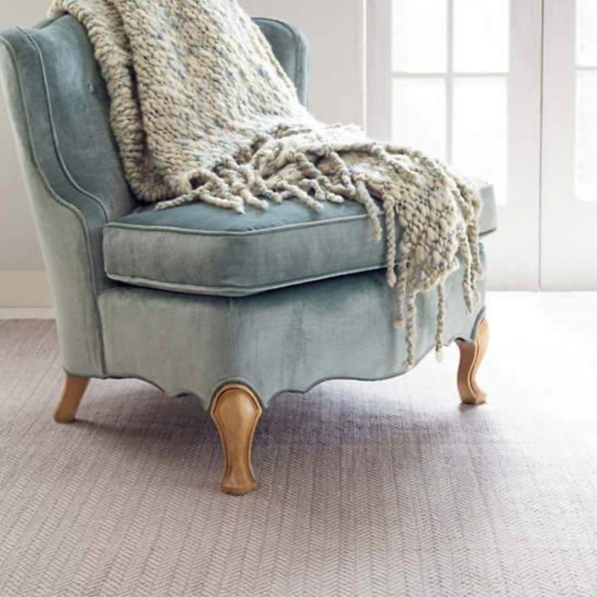 Herringbone Dove Grey Woven Cotton Rug styled under a blue chair. Styled view.