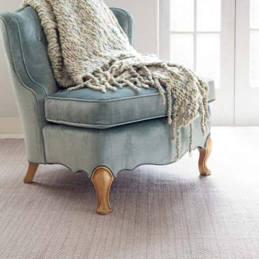 Herringbone Dove Grey Woven Cotton Rug styled under a blue chair. Styled view.