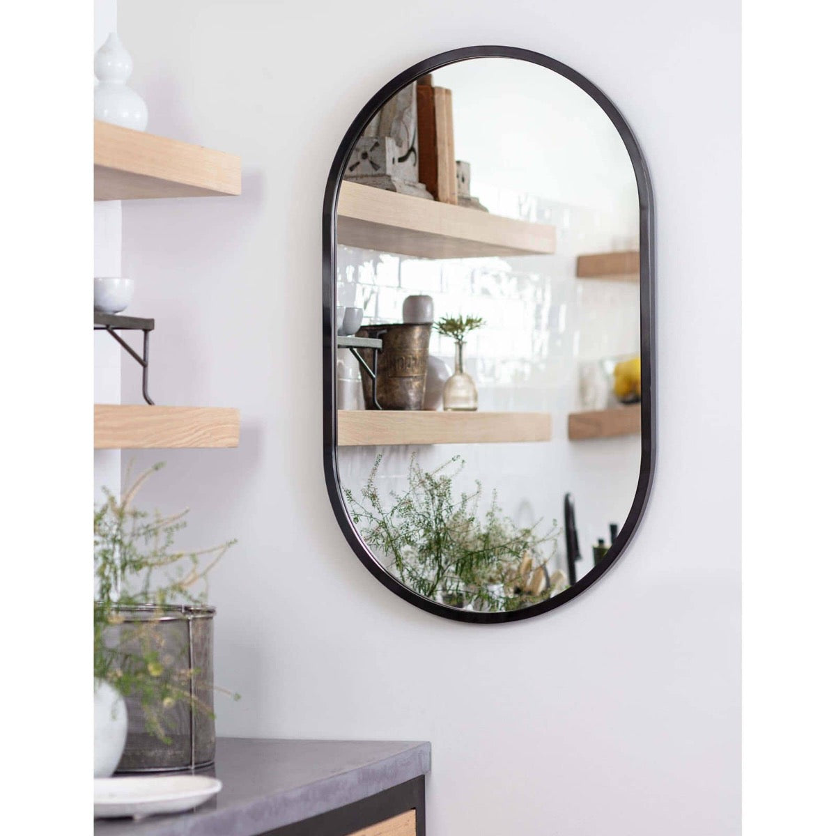 Josie Mirror Steel styled on a white wall with wood shelves. Styled view.