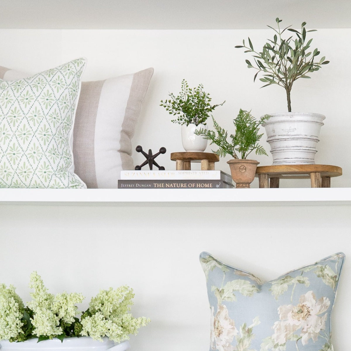 Leta Teak Stand styled with decor and pillows on white shelving. Styled view.