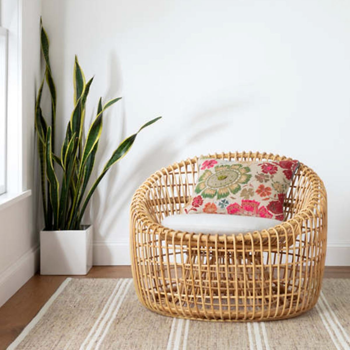 Malta Natural Woven Wool Rug styled under a wicker chair and planter. Styled view.