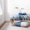 Marled Grey Woven Cotton Rug styled under a blue ottoman in a white room. Styled view.