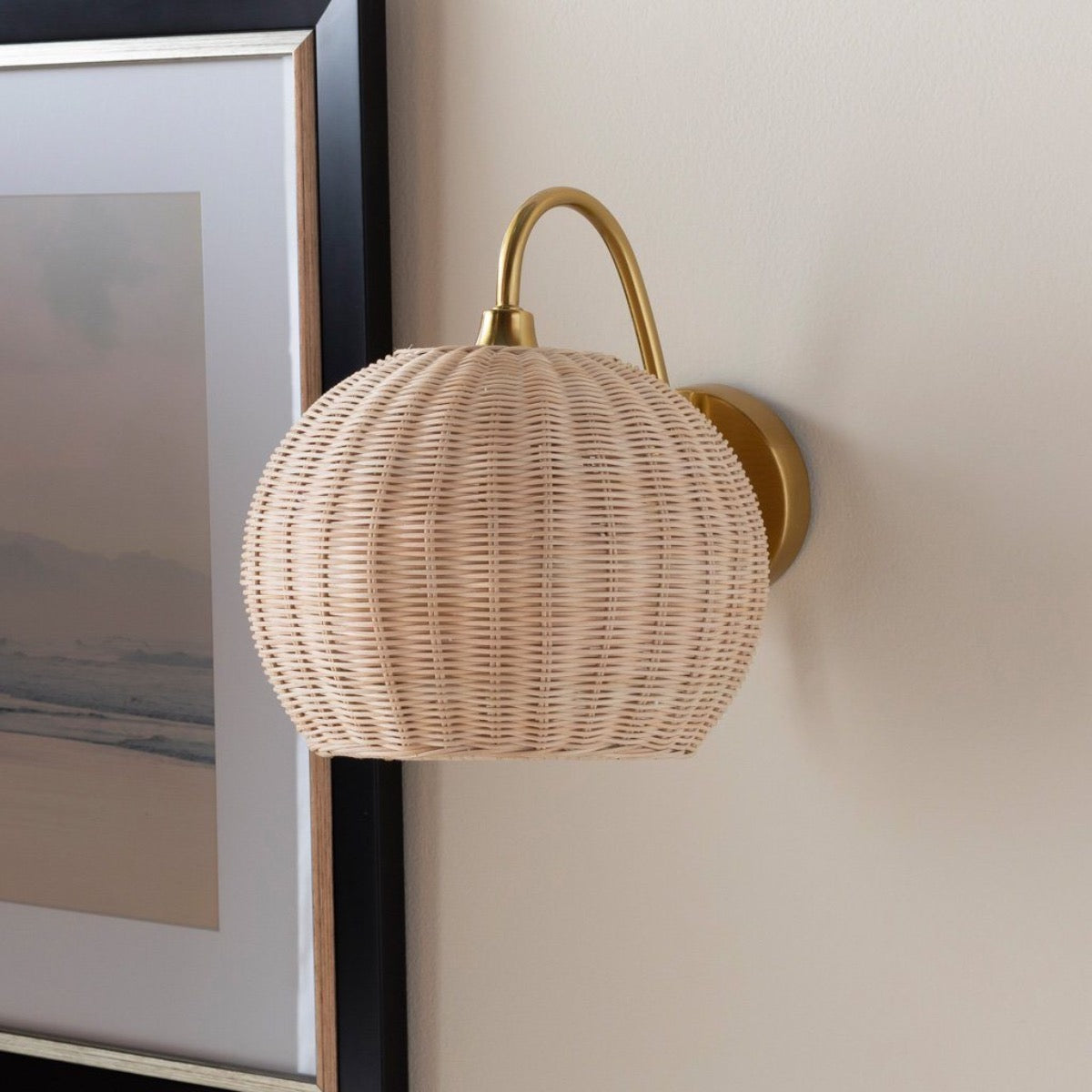 Marnie Rattan Wall Sconce styled on a neutral wall beside a painting. Styled view.