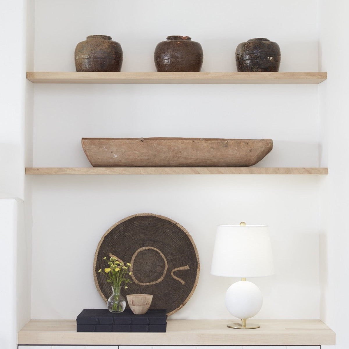 Megan Table Lamp styled on a wood surface with greenery and neutral shelving above. Styled view.