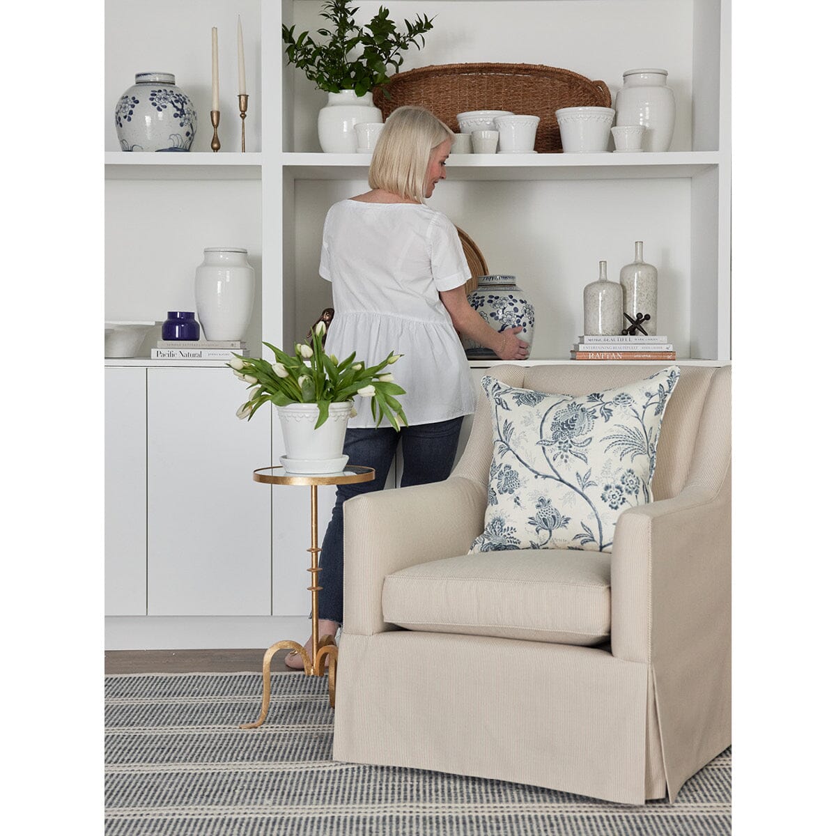 Owen Chair styled with a blue pillow and gold accent table against white shelving. Styled view.