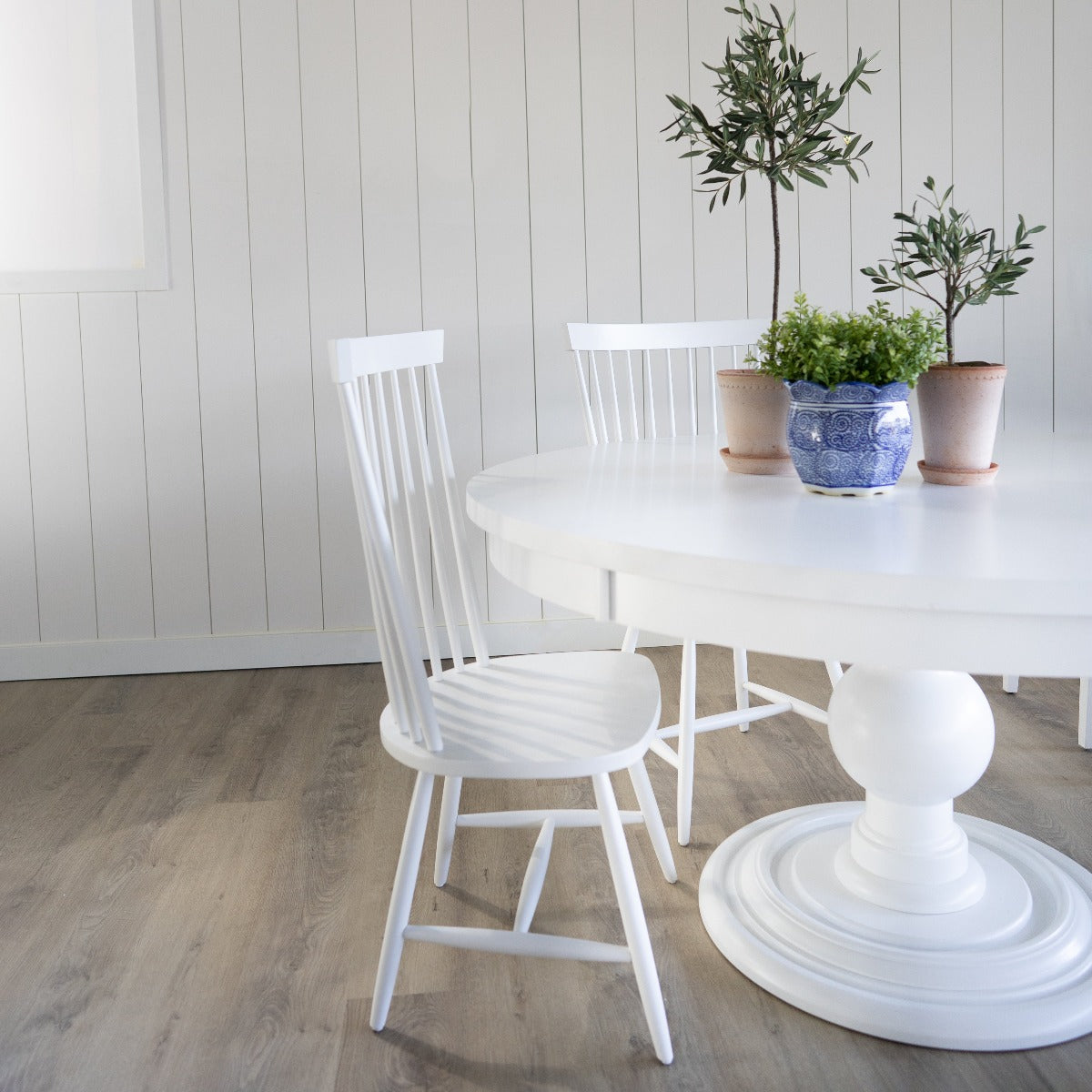 Pedestal Dining Table styled with white dining chairs and planters. Styled view.