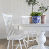 Pedestal Dining Table styled with white dining chairs and planters. Styled view.
