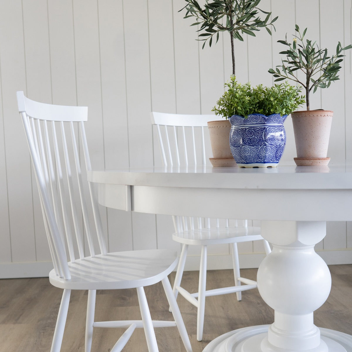 Pedestal Dining Table styled with white dining chairs and planters. Styled view.