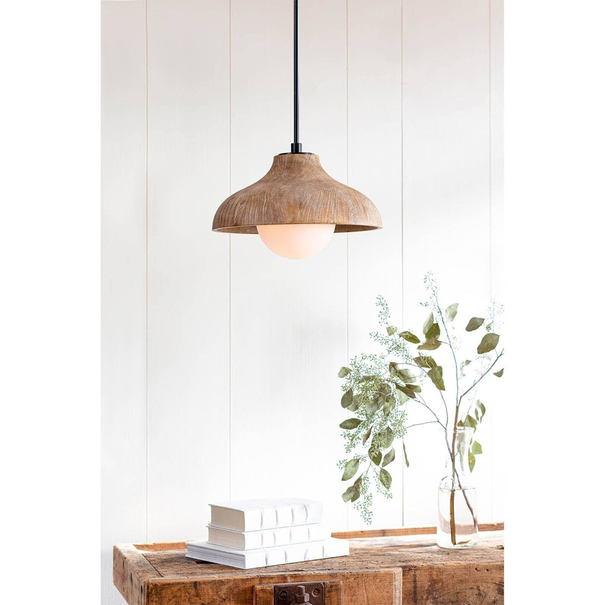 Surfside Wood Pendant styled over a wood table with books and greenery. Styled view.