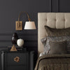 Rennie Swing-Arm Wall Sconce styled in a black wall beside a bed with dark decor. Styled view.