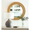 Rhode Rattan Mirror styled over a distressed table with lamp and greenery. Styled view.