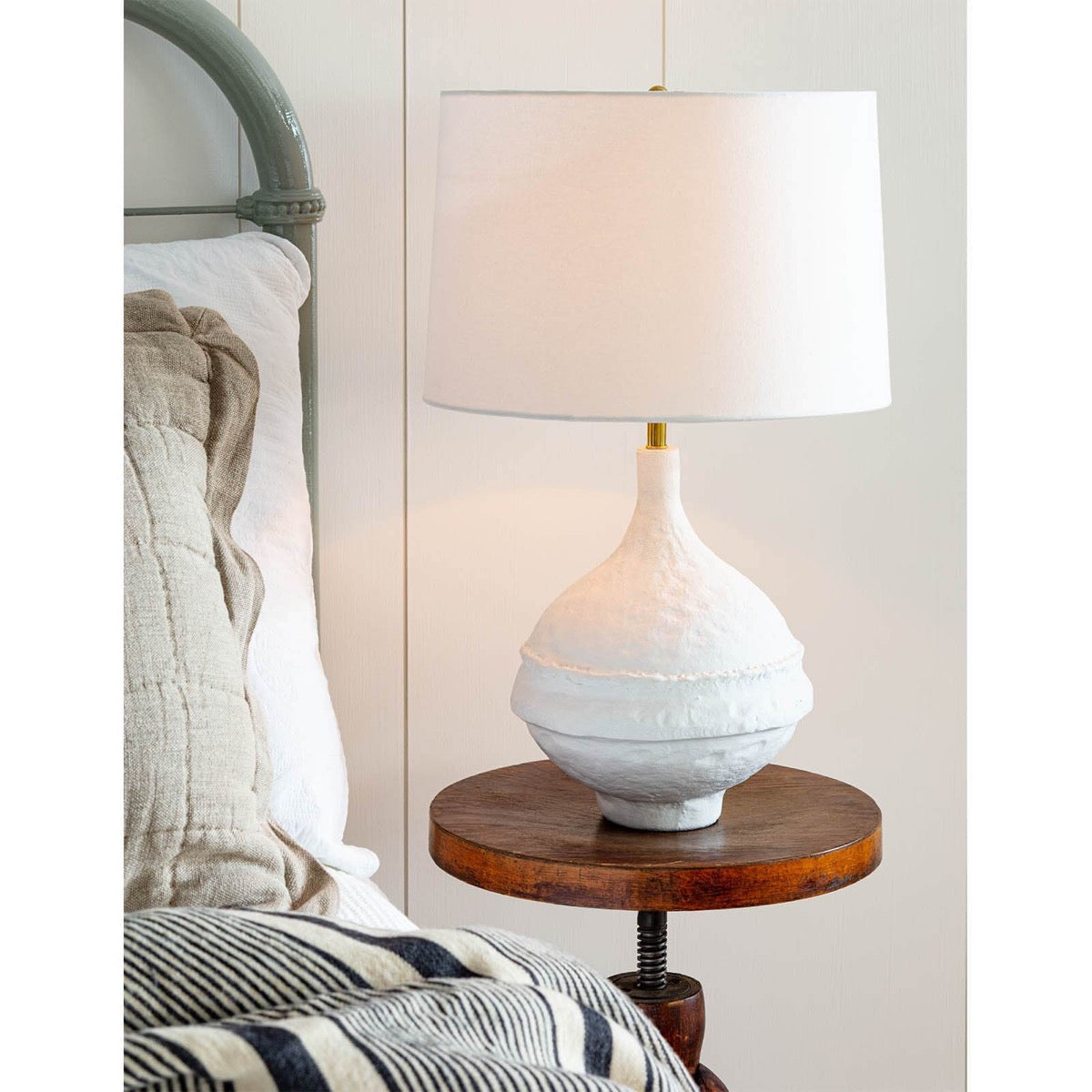 Viva Table Lamp styled on a wood table beside a green bed. Styled view.