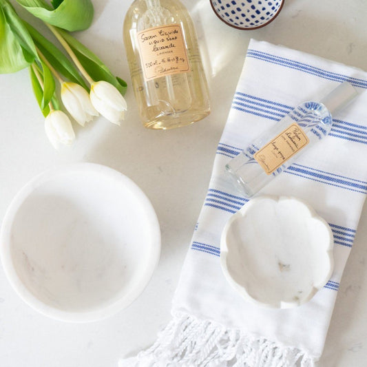 Round Marble Scalloped Bowl styled with soaps, florals and clothes in a bathroom. Styled view.