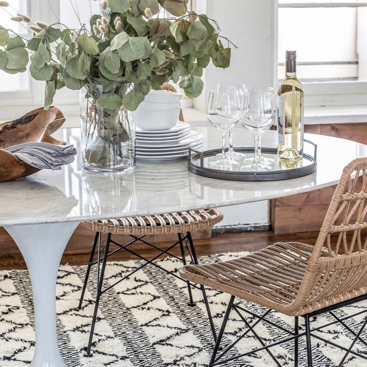 Trumpet Dining Table Oval with Marble Top - Large styled with wicker chairs, serveware and greenery. Styled view.