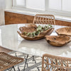 Trumpet Dining Table Oval with Marble Top - Large styled with wood bowls and wicker chairs. Styled view.
