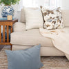 Twiggy Natural Woven Wool/Jute Rug styled under a cream sofa with accent pillows. Styled view.