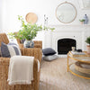 Twiggy Natural Woven Wool/Jute Rug styled in a white living room with wicker chairs and white mantel. Styled view.