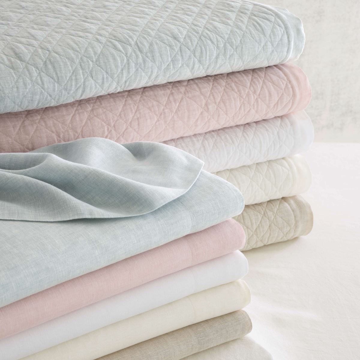 Folded stack of washed linen bedding in multiple colours. Styled view.