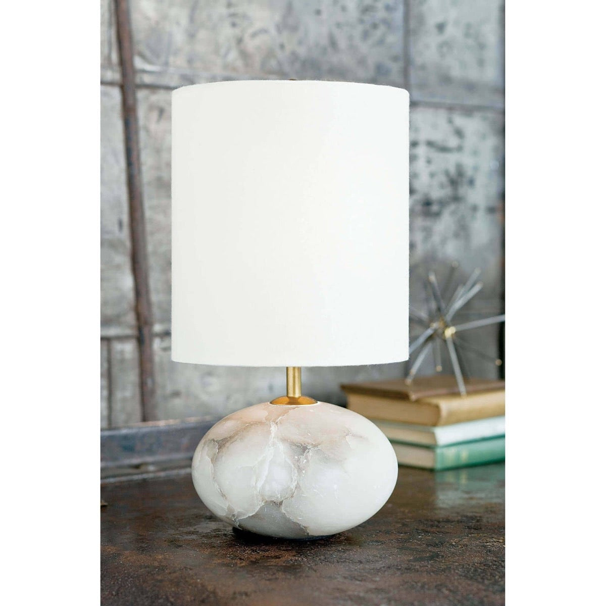 Alabaster Petite Orb Lamp styled on a dark surface with books and decor. Styled view.