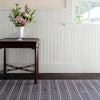 Archer Navy Woven Cotton Rug styled with a wood table in a panel white room. Styled view. 