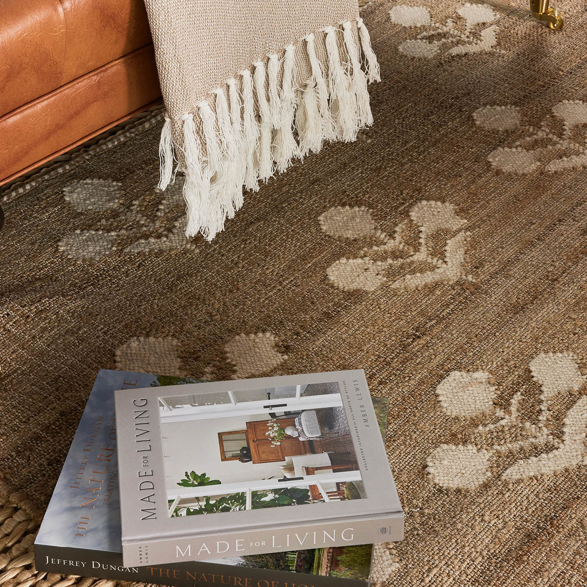 Bloom Jute Rug styled in a living room with leather coach and books. Styled view. 