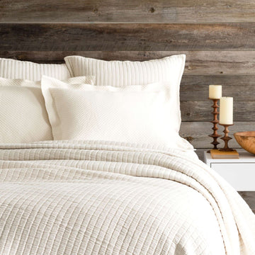 Bed with ivory coverlet and pillows. Styled view.