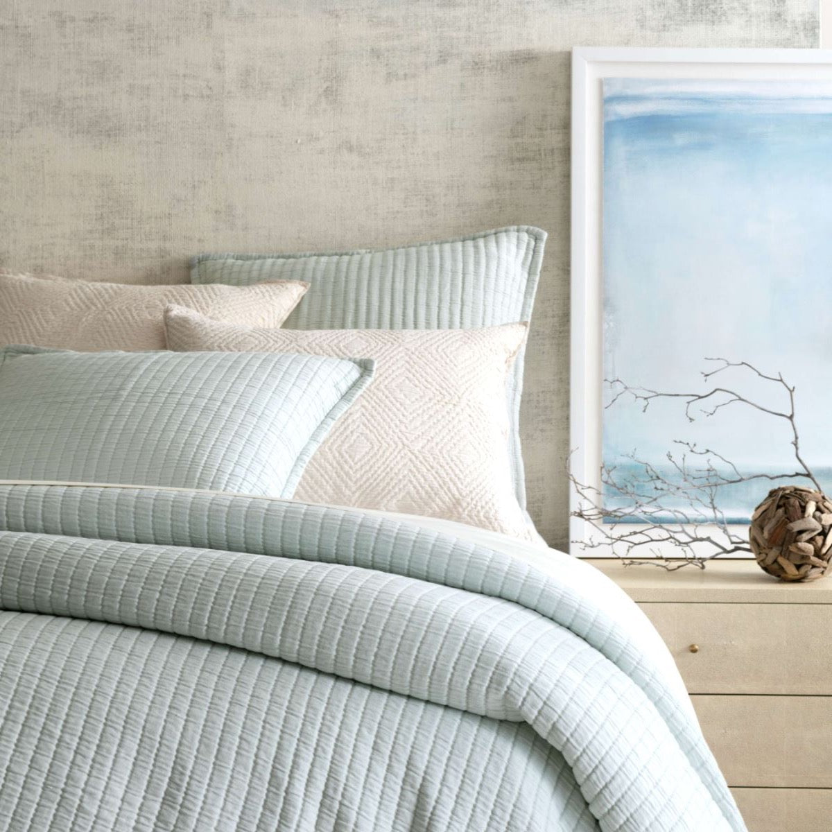 Bed with light blue coverlet and textured wall. Styled view.