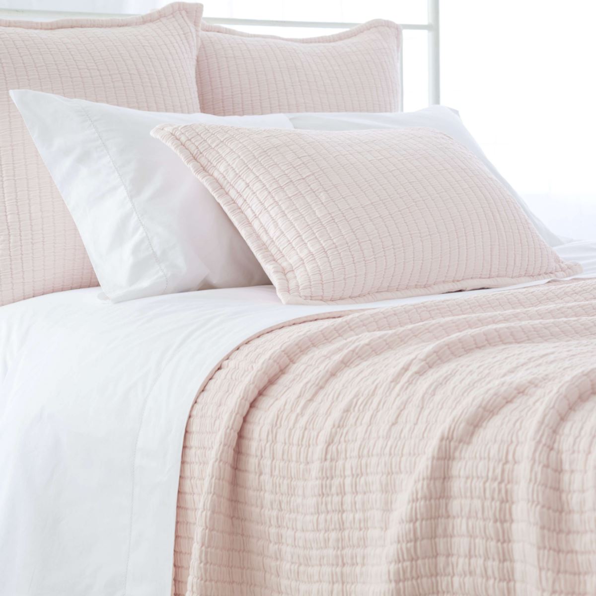 Light pink textured bedding styled with white sheets. Styled view.