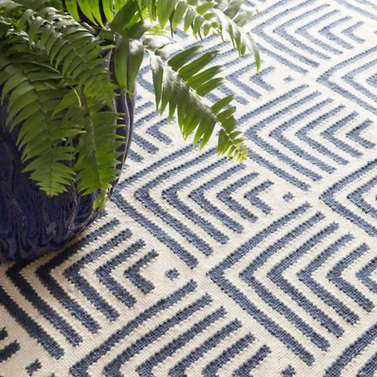 Cleo Navy Indoor/Outdoor Rug styled under a blue potted plant. Styled view. 