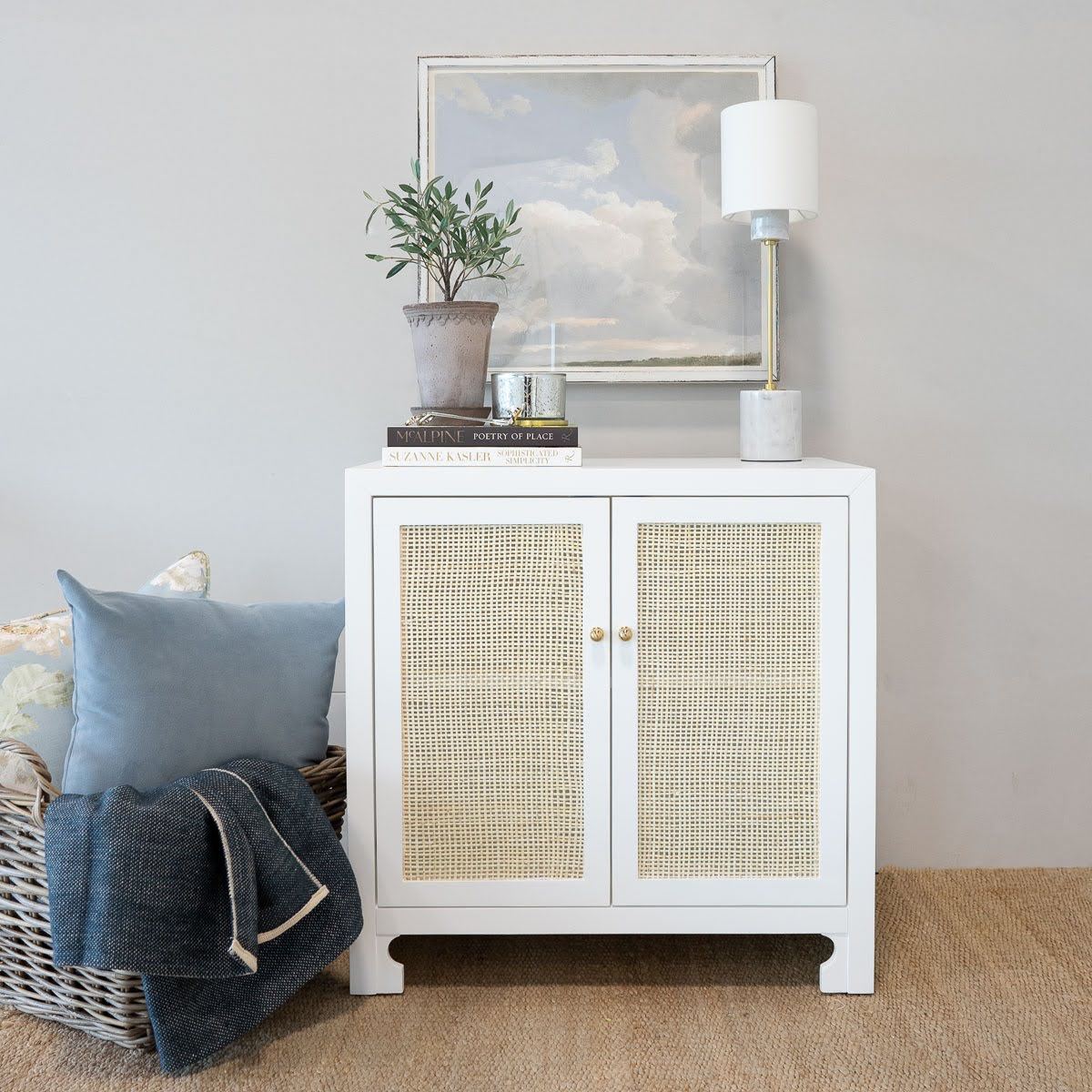 Colette Occasional Cabinet styled with decor and a lamp and blue bedding. Styled view.