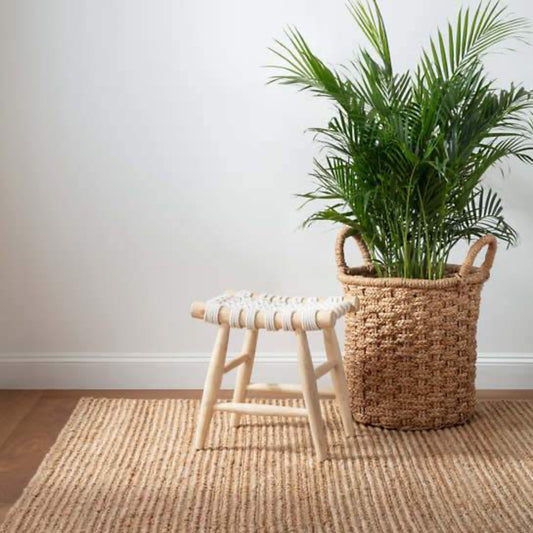 Dunes Natural Woven Jute Rug styled with a stool and woven basket. Styled view. 