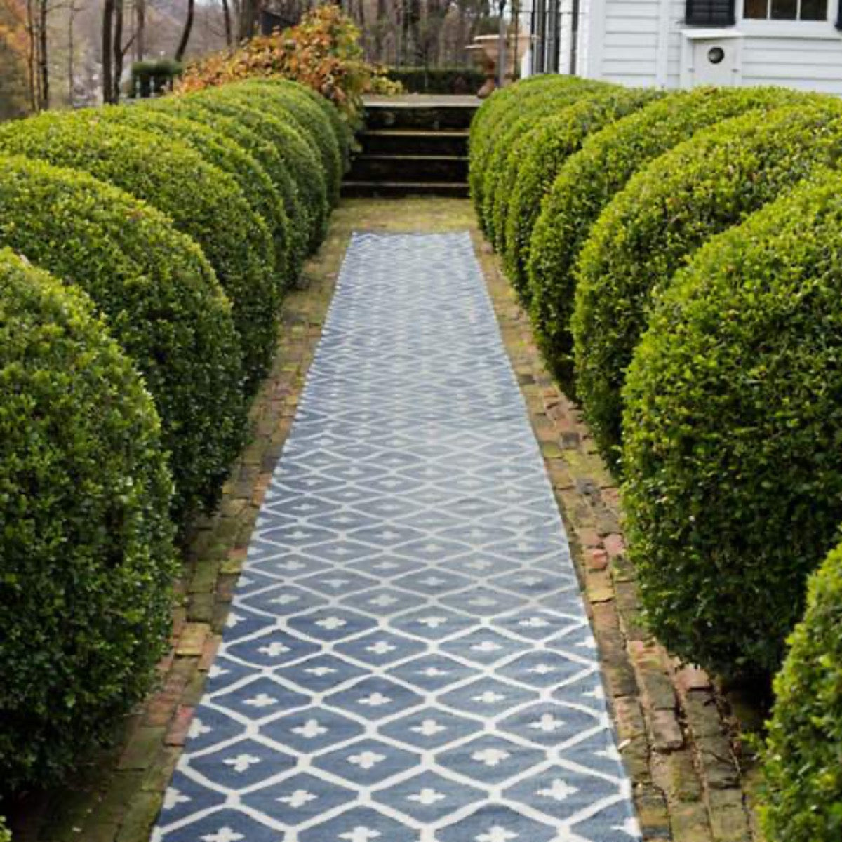 Elizabeth Navy Indoor/Outdoor Rugs styled outdoors down a pathway with shrubbery. Styled view. 