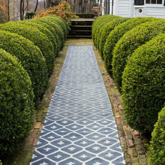 Elizabeth Navy Indoor/Outdoor Rugs styled outdoors down a pathway with shrubbery. Styled view. 