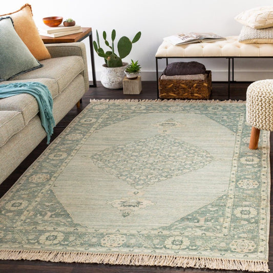 Ella Rug styled with a grey sofa, neutral stool and greenery. Styled view. 