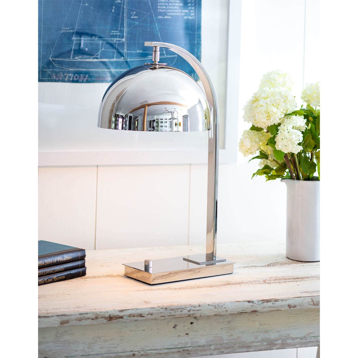 Harwich Desk Lamp styled on a wood console with books and greenery. Styled view.