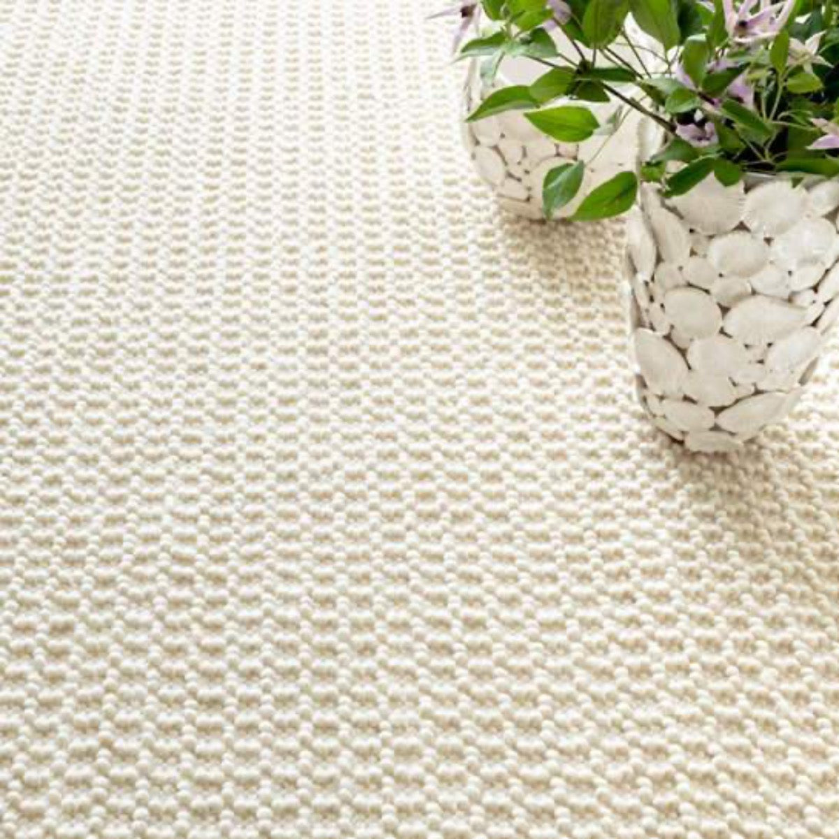 Hooper Woven Wool Rug styled with white vases and greenery. Styled view. 